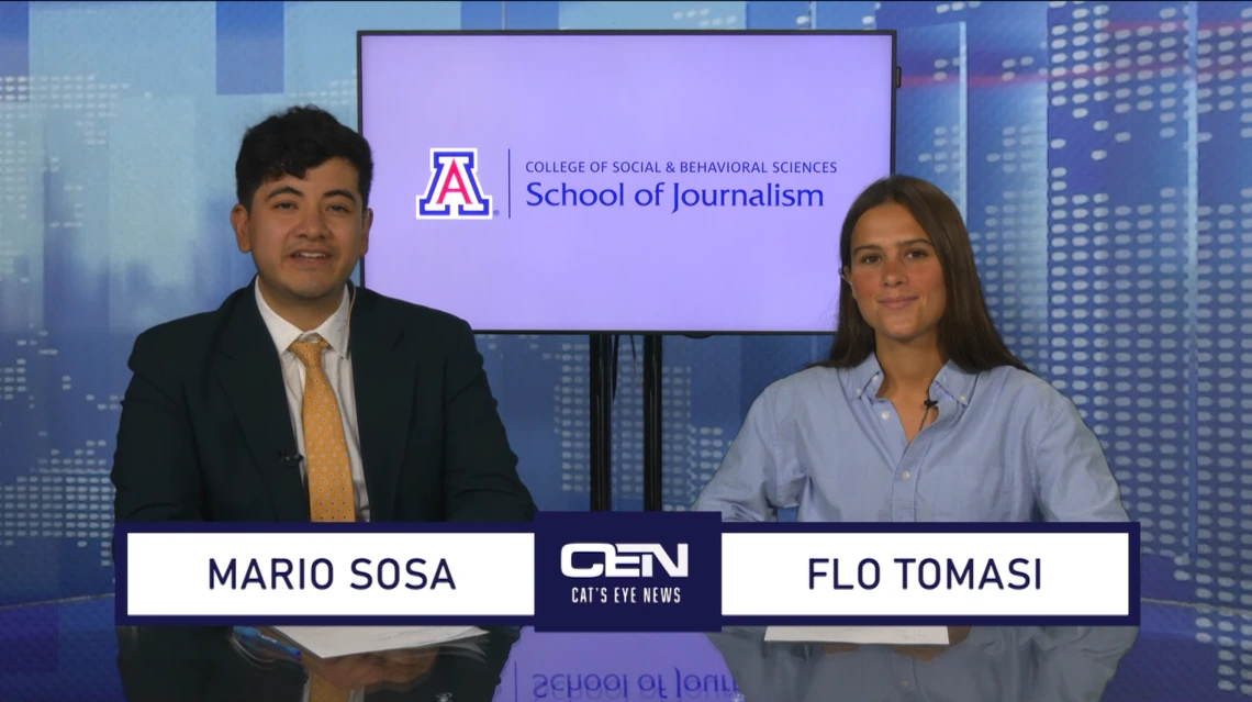 Two students sit at the anchor desk in a studio