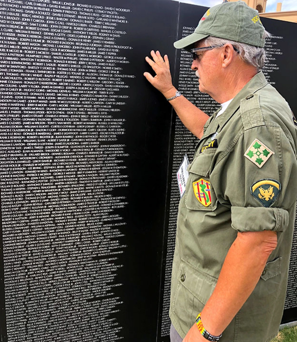 Older man in uniform touching names on war memorial