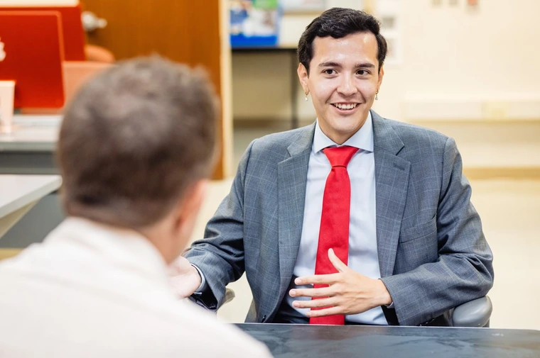 A student dressed in a business suit interviews with a media partner at the Fall 2023 Internship Fair in