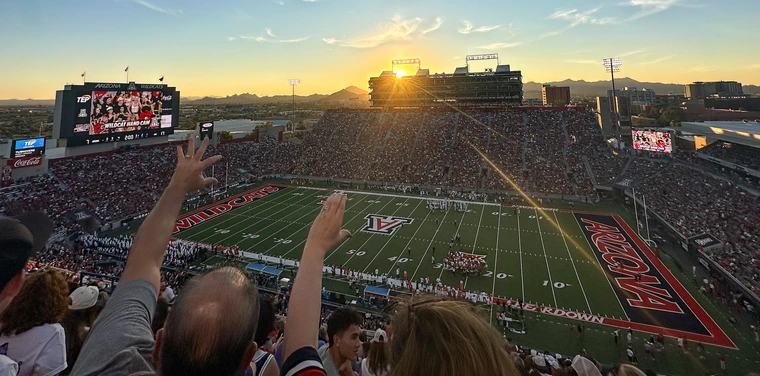 Arizona Stadium fans cheer while the sun sets in the background