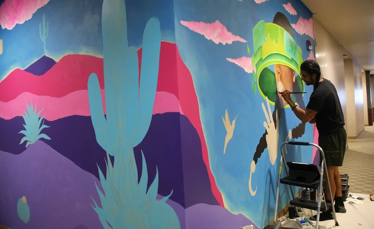 A artist paints on a wall in a hallway