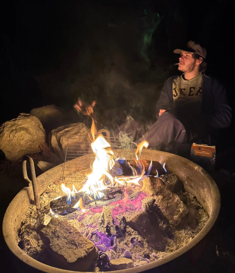 A person sits next to a campfire at night