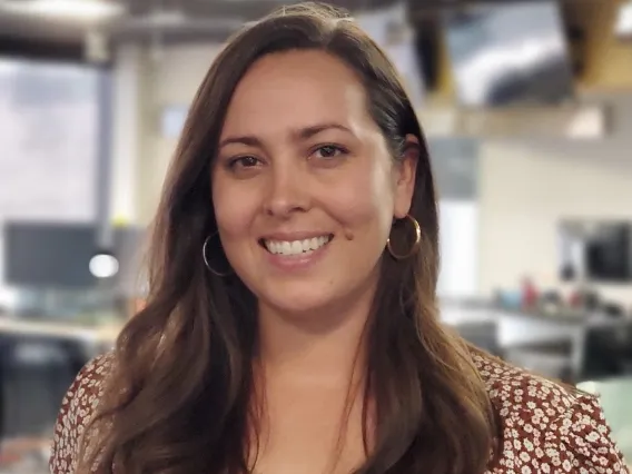 A woman with long brown hair stands in front of an office space.