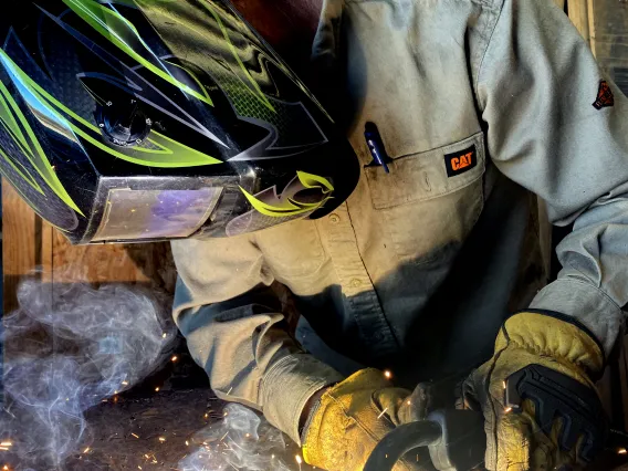 A man wearing a face-covering welding mask while doing metal work.