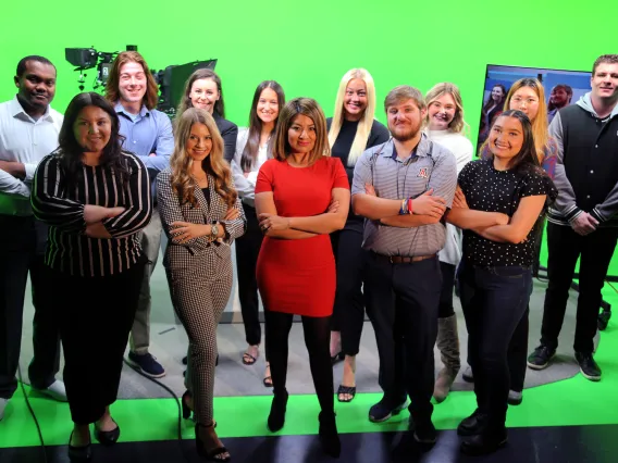 Students gather at broadcast desk with Prof. Soto