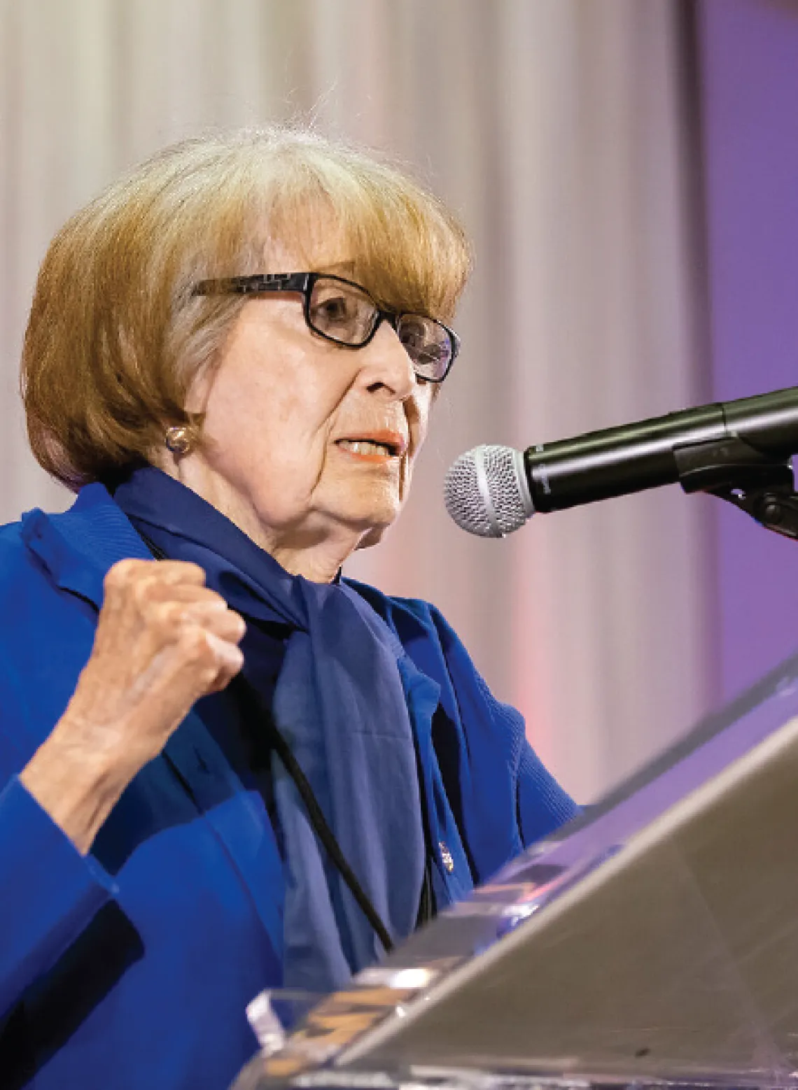 Edith Auslander speaks into a microphone wearing a blue suit top.