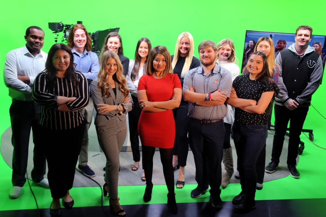 Students gather at broadcast desk with Prof. Soto