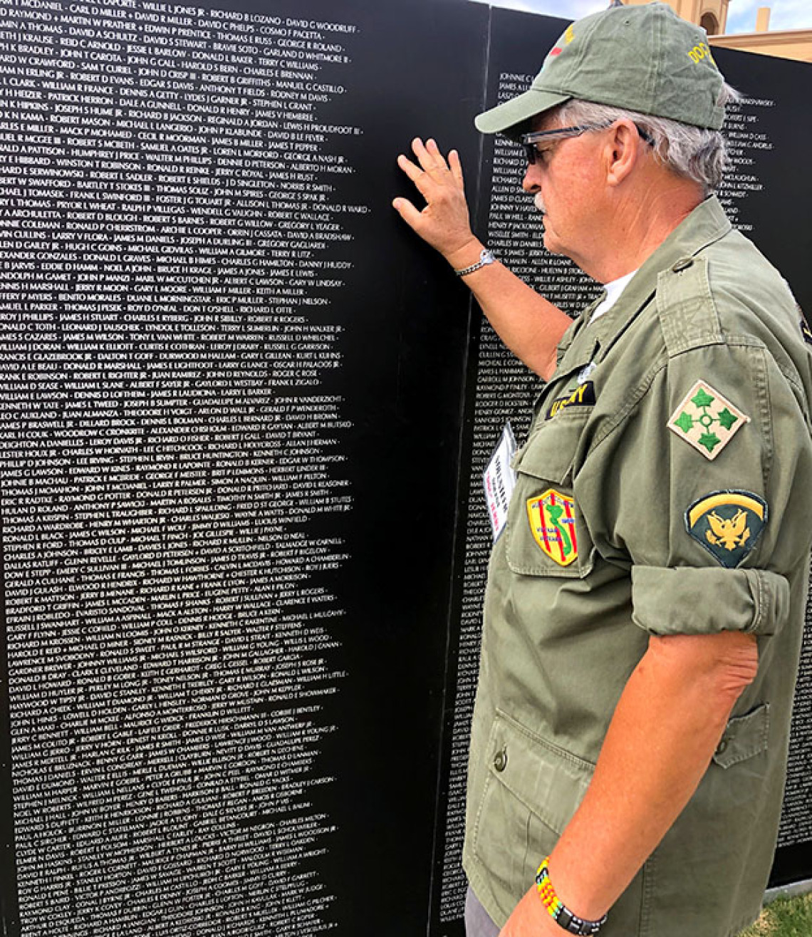 Older man in uniform touching names on war memorial