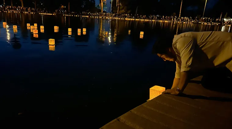 A man lays a floating lantern in a pond 