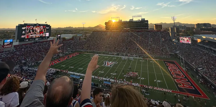 Arizona Stadium fans cheer while the sun sets in the background