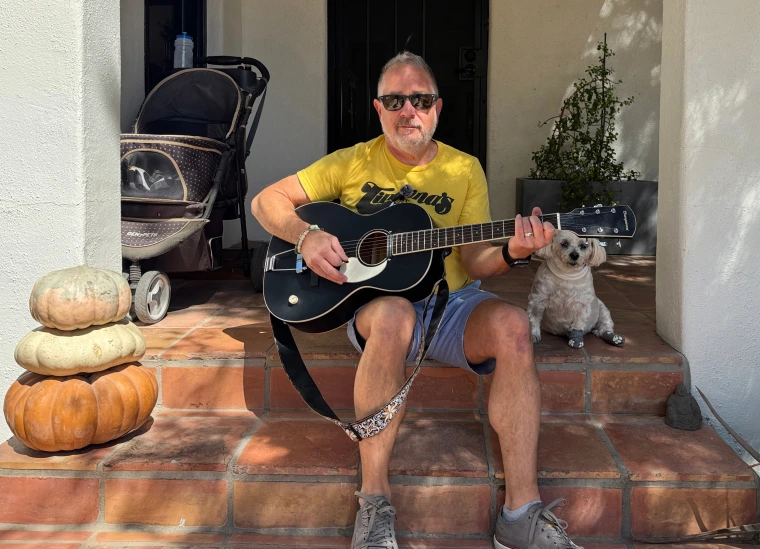 A man stums a guitar on his porch