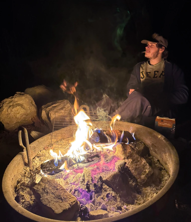 A person sits next to a campfire at night