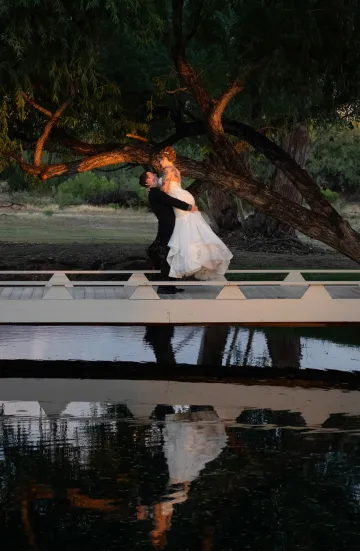 A bride and groom embrace outdoors under a large tree