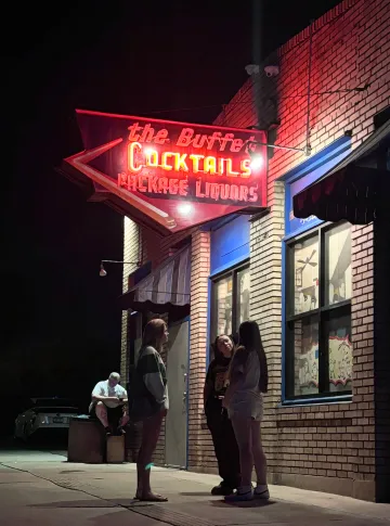 People stand below a neon sign at night